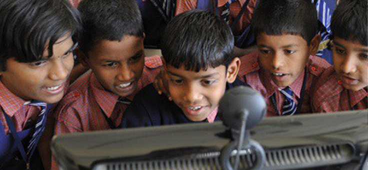 Imagem mostra cinco garotos sorrindo em frente a um computador