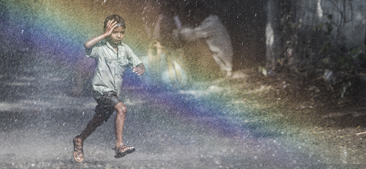 Cena do filme Lion mostra um menino correndo pela chuva e um arco-íris ao fundo