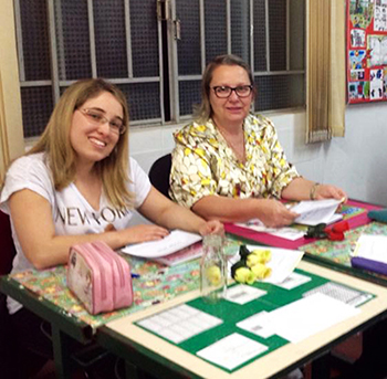 Educadora Rosângela Thomazino Mendes, à direita, sentada em mesa na escola EstadualProfessor Irineu Tobias