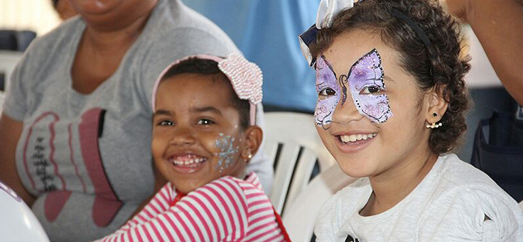 Duas crianças sorrindo. Uma delas está com uma borboleta desenhada no rosto