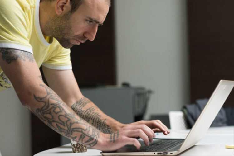 Foto de perfil de homem debruçado sobre mesa usando notebook