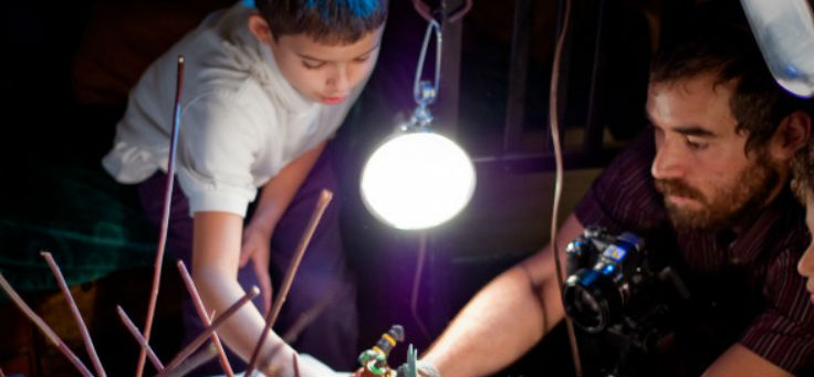 Um adulto e uma criança brincam com bonecos de RPG sob a luz de uma lanterna.