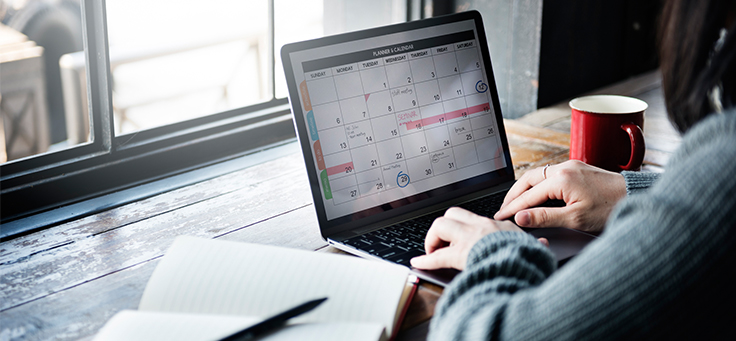 Mulher olha para computador em que aparece a imagem de um calendário.