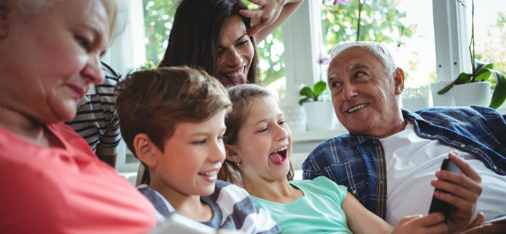 Duas crianças sorriem ao segurar um smartphone, assim como um idoso e uma mulher adulta