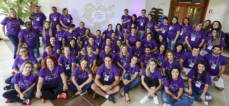 Mais de 20 colaboradores do Programa de Voluntariado da Fundação Telefônica Vivo aparecem agrupados, usando camiseta púrpura e sorrindo para foto