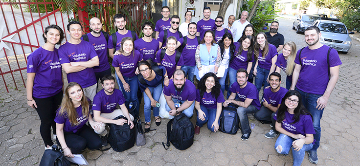 Imagem mostra pessoas usando camiseta roxa onde se lê Voluntários Telefônica em ação com trainees