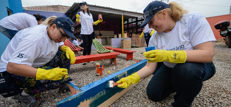 Três voluntários pintam área de recreação em uma instituição, durante o Dia dos Voluntariados