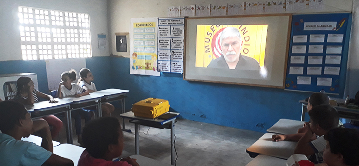 Na imagem alunos do professor Isaias estão sentados em roda em sala de aula, assistindo a vídeo em etapa de projeto que alia leitura, tecnologia e pesquisa.