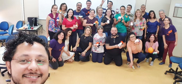 Grupo com homens e mulheres posa em sala de aula, segurando material de formação da Assessoria Inova Escola, que promove inovação educativa na rede pública, em Goiás.