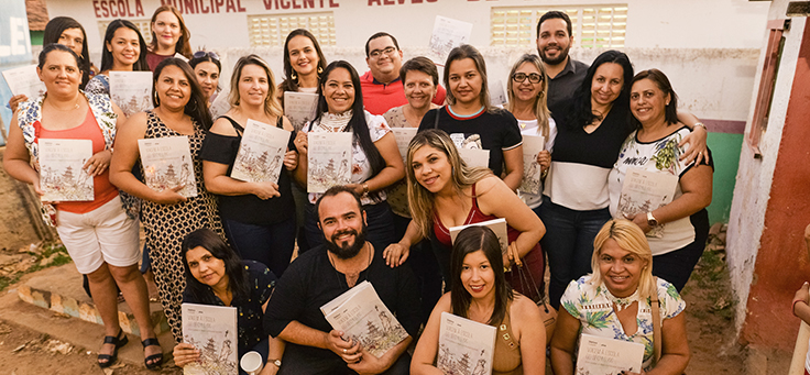 Educadores e formadores responsáveis pelo caderno que reúne boas práticas educacionais de Saloá-PE seguram a publicação e posam agrupados para a foto.