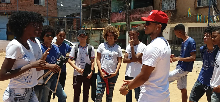 Alunos estão em volta do jogador Rogério Xodó, entrevistado em documentário descrito no e-book com práticas pedagógicas do CENOR, em campo do bairro Arenoso.