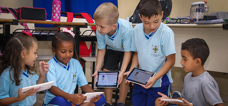 Cinco crianças estão segurando tablets em sala de aula da EMEF Presidente João Goulart, em Viamão (RS), durante ação do Aula Digital, programa que promove a inclusão digital.