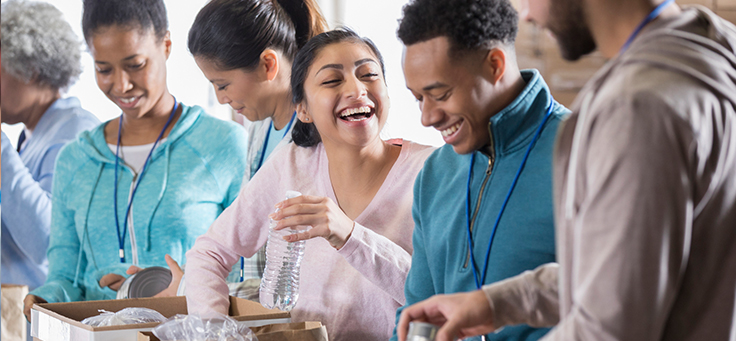 Imagem mostra grupo de pessoas sorrindo enquanto tiram mantimentos da caixa de papelão (voluntariado internacional)