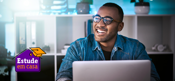 Homem de óculos está sorrindo sentado à frente de umcomputador para ilustrar pauta que traz uma lista de recursos digitais de aprendizagem para professores, estudantes e pais.