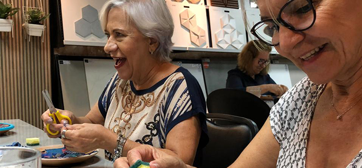 Imagem mostra duas mulheres sorrindo enquanto manuseiam alguns pedaços de pano