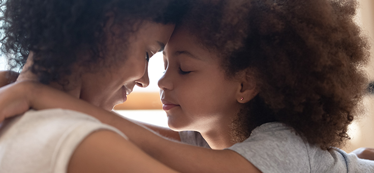 Imagem de mãe e filha se abraçando frente a frente com os olhos fechados e as testas juntas uma da outra