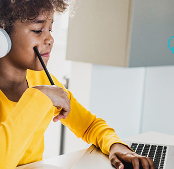 A imagem mostra uma criança usando fones de ouvido enquanto olha para a tela de um notebook para ilustrar pauta sobre a Hora do Código e a promoção da cultura digital. Ela é negra, tem cabelos encaracolados e usa uma blusa amarela.