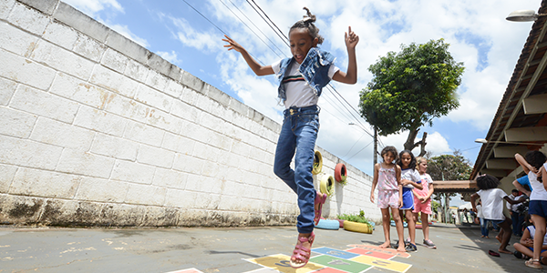 Criança brinca de amarelinha enquanto outras crianças estão atrás dela esperanda a vez em uma escola atendida pelo projeto Aula Digital ProFuturo em Goiânia