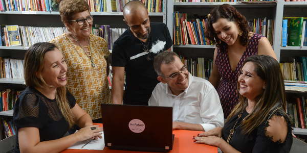 Educadores do projeto Aula Digital ProFuturo em Goiânia reunidos em uma sala da escola onde se vê uma estande com livros atrás deles