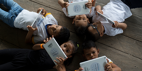 Crianças em Manaus que fazem do projeto Aula Digital ProFuturo seguram tablets do projeto enquanto estão deitadas no chão