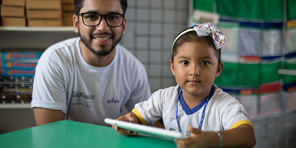 formador do Aula Digital Profuturo em Manaus posa para foto ao lado de uma criança que segura o tablet do projeto