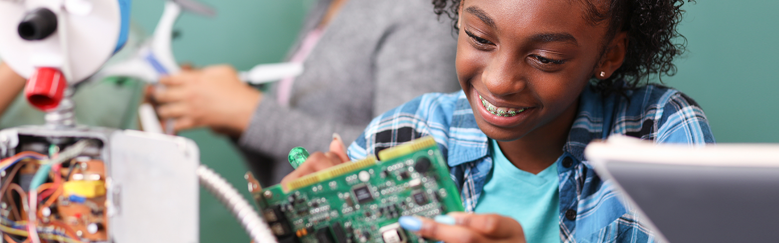 Jovem manuseia uma peça mecânica de computador em aula de robótica e programação