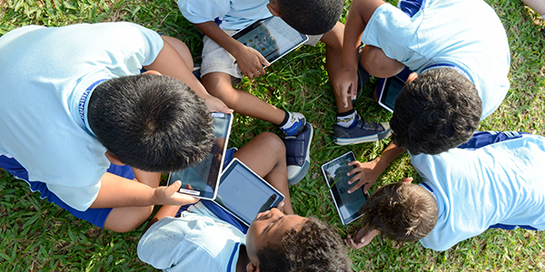 Crianças atendidas pelo projeto Aula Digital ProFuturo em Viamão estão sentadas na grama manuseando os tablets do projeto.