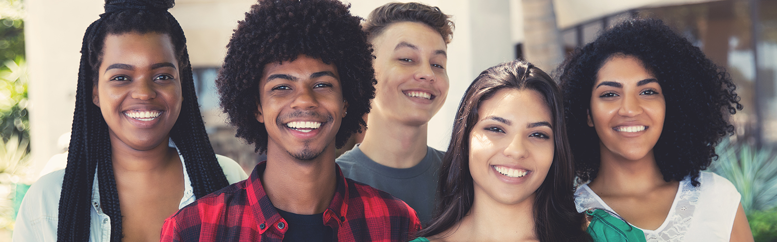 Imagem mostra um grupo de cinco jovens em pé, um ao lado do outro. Eles sorriem enquanto posam para a foto