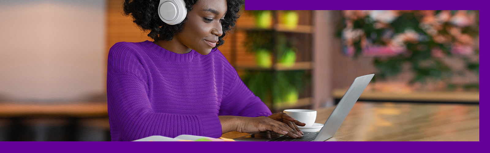 Uma professora negra, usando uma blusa púrpura e fones de ouvido usa um notebook para acessar os cursos da plataforma Escolas Conectadas