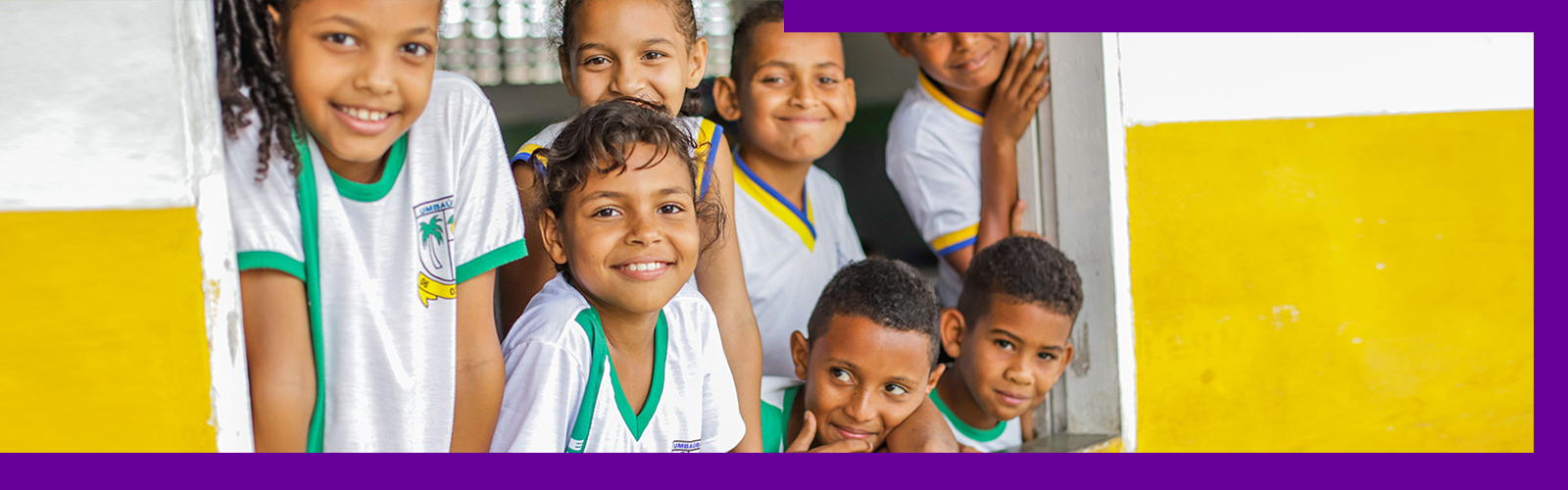 Imagem mostra menina de uniforme escolar sorrindo segurando um tablet onde se vê o logotipo do Profuturo Aula Digital