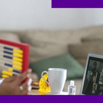 A imagem mostra uma mulher na sala de sua casa, sentada em frente a uma mesa onde está um computador, um ábaco e uma xícara de porcelana. Ela está olhando para tela e interagindo com um grupo de pessoas em uma videoconferência