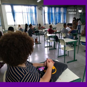 A pauta Educar é realizar traz a imagem de uma sala de aula em que um grupo de aproximadamente dez pessoas estão sentadas em carteiras olhando para três educadoras que estão afrente da sala, próximas à lousa.