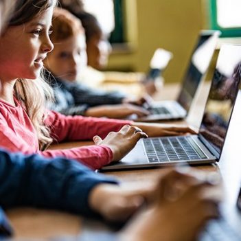 Imagem de várias crianças em uma sala com computadores sobre a mesa