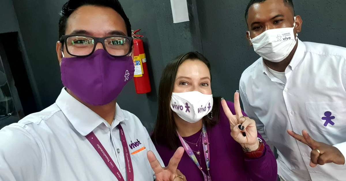 Imagem mostra três voluntários, sendo dois homens e uma mulher. Eles usam máscara e sorriem para a foto.