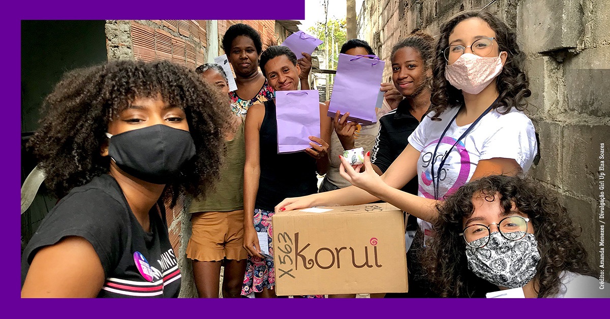 Imagem mostra grupo de meninas do coletivo Girl Up Elza Soares fazendo a doação de absorventes para mulheres de uma comunidade do Rio de Janeiro. É possível ver oito mulheres na imagem.