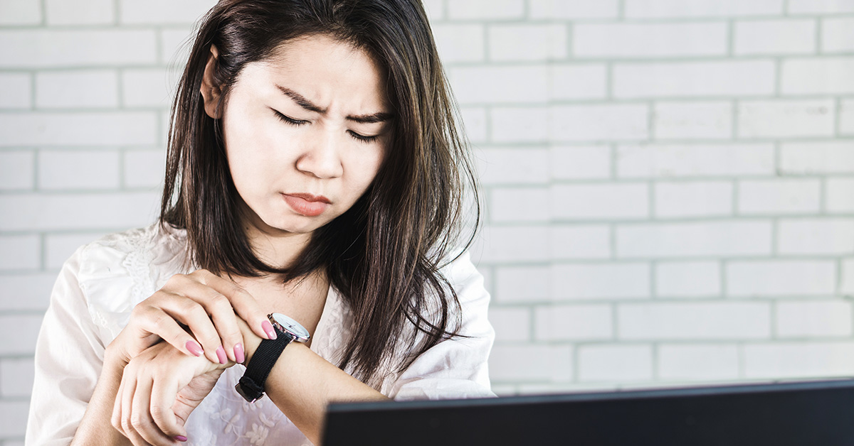 Na imagem uma mulher jovem está olhando para o relógio com cara fechada, como quem briga contra o tempo, para retratar pauta sobre procrastinação