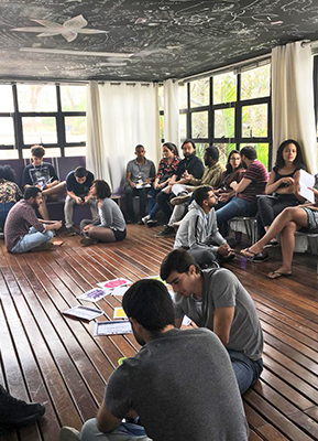 Jovens empreendedores estão sentados no chão, em grupos de cinco pessoas debatendo durante dinâmica da imersão do Pense Grande