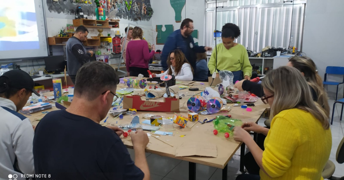 Professores reunidos em torno de uma mesa com sucatas diversas para a construção de protótipos eletrônicos em formação docente em robótica educacional