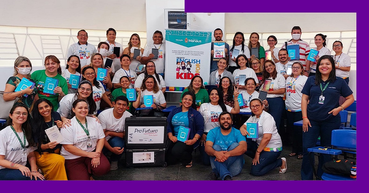 Imagem mostra grupo de educadores de Manaus reunidos em uma sala de aula. Entre eles, é possível ver a maleta do Aula Digital e um banner com o nome do projeto English for Kids