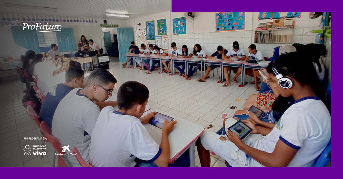 Imagem mostra um grupo de estudantes em sala de aula utilizando tablets e fones de ouvido