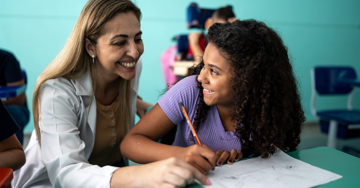 Professora apoia estudante em sala de aula.