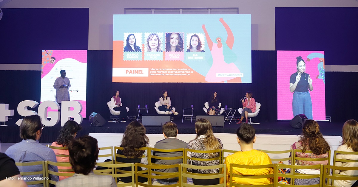 Imagem mostra o palco onde aconteceu o festival social good brasil, com quatro palestrantes sentadas. Há telões e também é possível ver a plateia