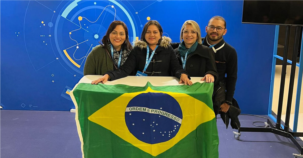 Imagem mostra quatro professores, três mulheres e um homem, em pé, segurando a bandeira do Brasil. Ao fundo se vê um fundo azul com o logotipo do evento enlightED 2022.