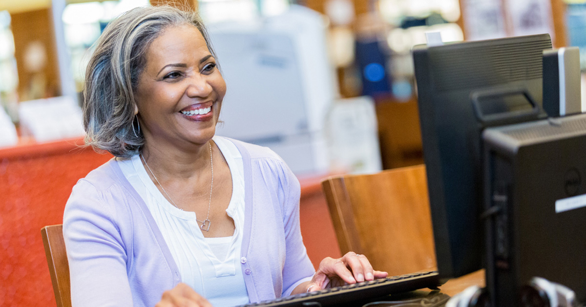 Na imagem, já uma professora negra utilizando um computador. Ela tem cabelos brancos e lisos