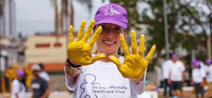 Imagem mostra uma moça olhando para a câmera e mostrando as palmas das duas mãos, pintadas de amarelo