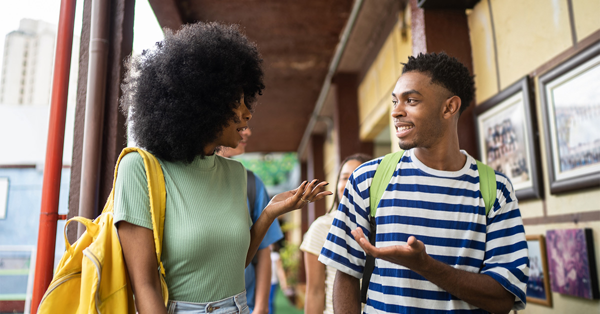 Imagem mostra dois jovens estudantes negros conversando e andando por um corredor.