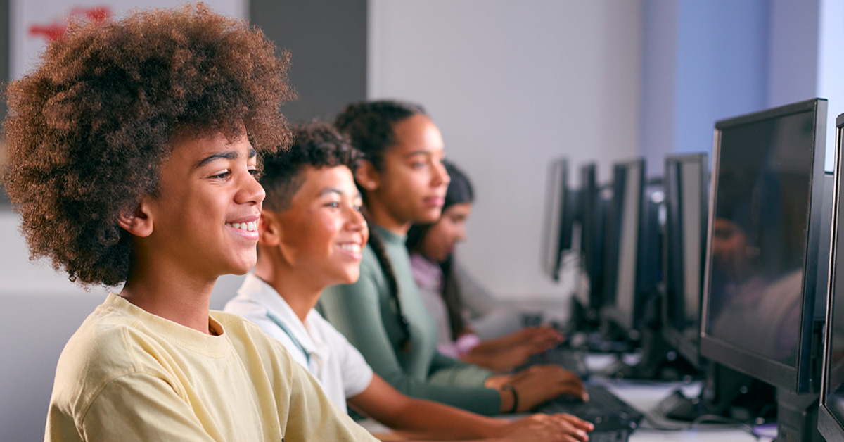 Imagem mostra quatro estudantes em perspectiva, todos estão em sala de aula utilizando computadores