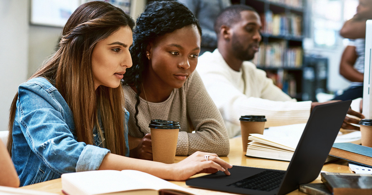 Imagem mostra três jovens em uma sala de estudos utilizando notebook. Dois jovens são negros e uma é branca