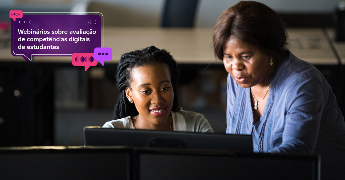 Imagem mostra uma educadora e uma estudante em sala de aula, utilizando computador, ambas são negras. A professora está mostrando algo para a aluna na tela do computador