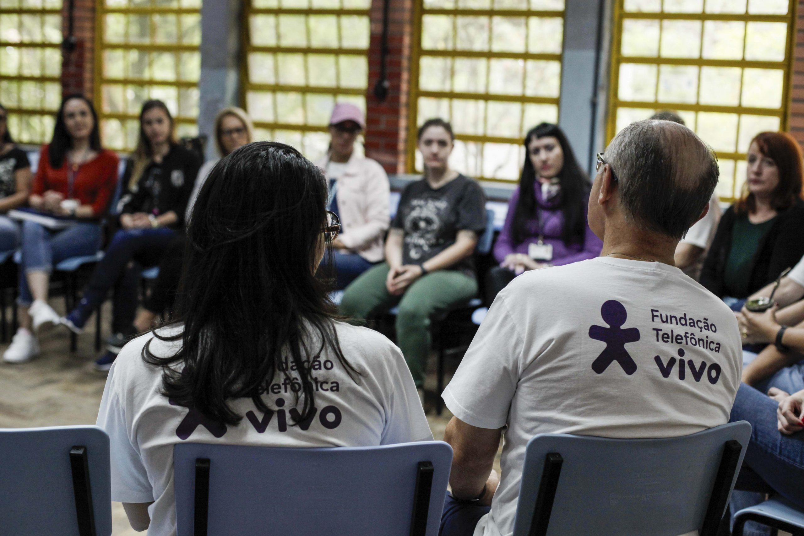 Voluntários na sala de aula, sentados em cadeiras dispostas em formato de círculo.